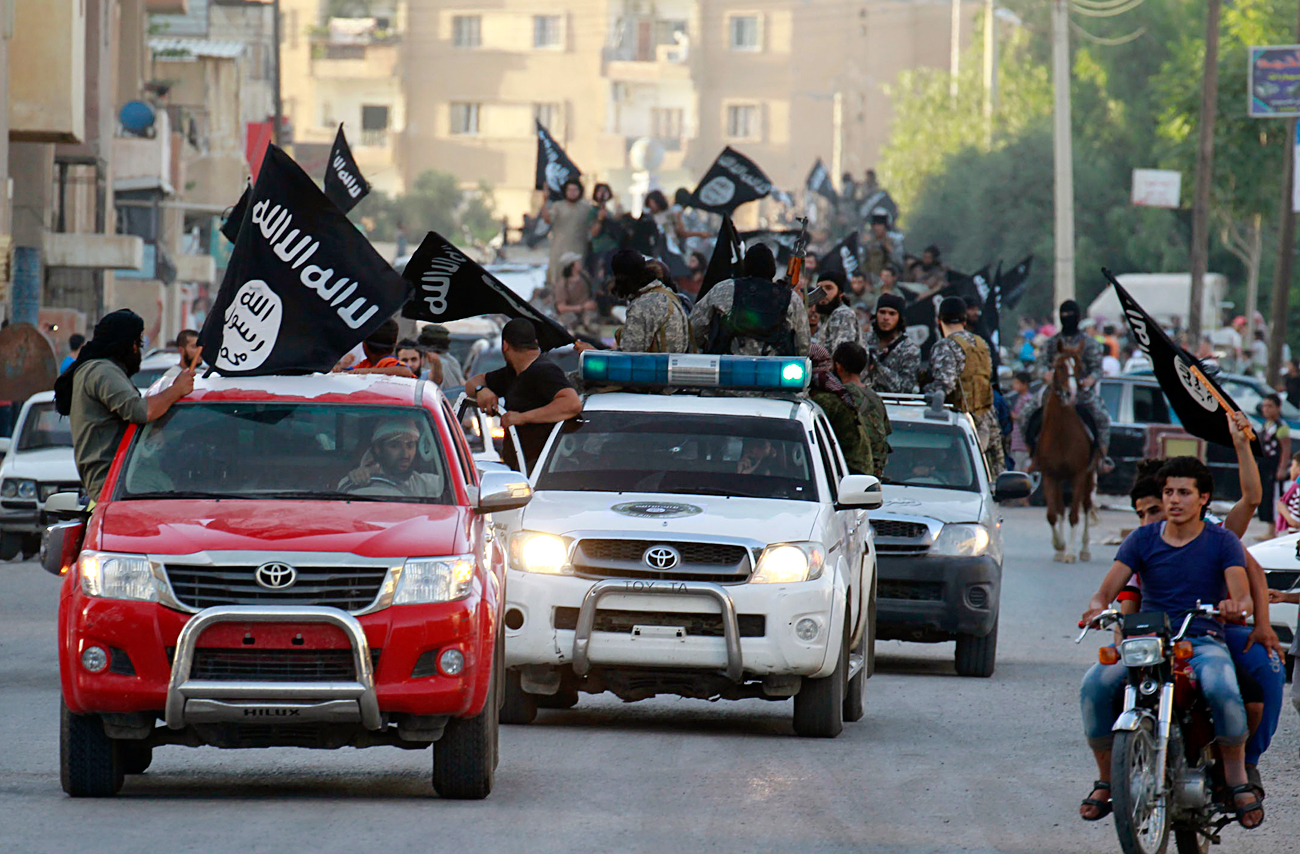 Ислямистки бойци развяват знамена от автомобили по време на военен парад по улиците на северната сирийска провинция Рака на 30 юни 2014 година. Бойците организираха парада в чест на обявяването на ислямски „халифат“, след като групировката превзе територия в съседен Ирак, съобщиха от служба за наблюдение. Ислямска държава, клон на Ал-Кайда, известна по-рано като Ислямска държава в Ирак и Леванта (ИДИЛ), в неделя публикува в интернет снимки на хора, развяващи черни знамена от автомобили с оръжия, вдигнати във въздухоа, обявиха от SITE. Снимката е направена на 30 юни 2014 година.