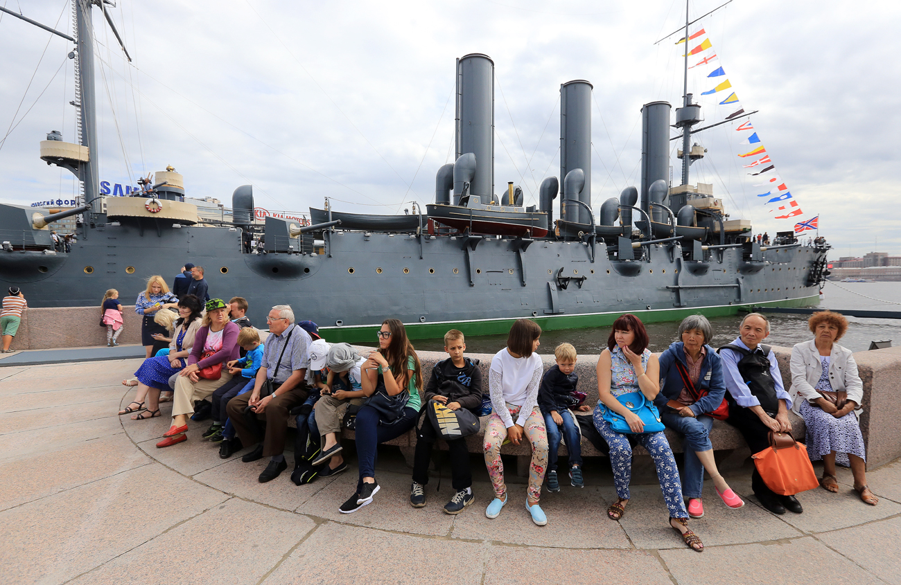 People sit in front of the Russian Aurora cruiser, Aug. 3, 2016.  Its new exhibition has been renewed during scheduled maintenance of the cruiser and is now dedicated not only to the October Revolution of 1917, but to the history of the Russian Navy. 