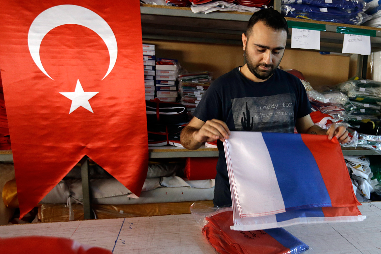 An employee of a flag-making factory folds a Russian flag as a Turkish flag adorns the display at left, in Istanbul, Tuesday, Aug. 9, 2016. The Factory production of flags has increased tenfold according to employees, as the public clamber to flay the national emblem which has become a symbol of support for the government during daily demonstrations to celebrate the suppression of a military coup. Turkey's President Recep Tayyip Erdogan arrives in Russia Tuesday for his first overseas trip since the coup attempt