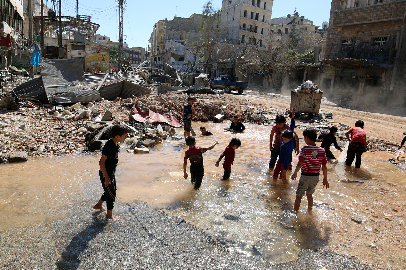 Деца си играят с водата от взривен водопровод в Алепо.