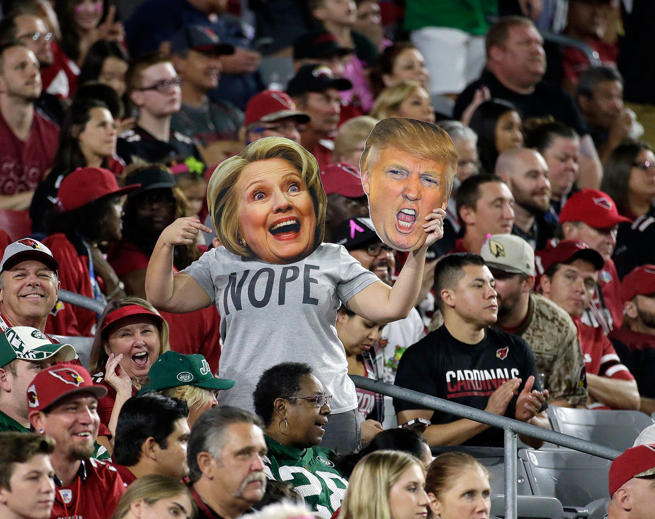 A fan wears a Hillary Clinton and holds a Donald Trump masks during the first half of an NFL football game between the New York Jets and the Arizona Cardinals.
