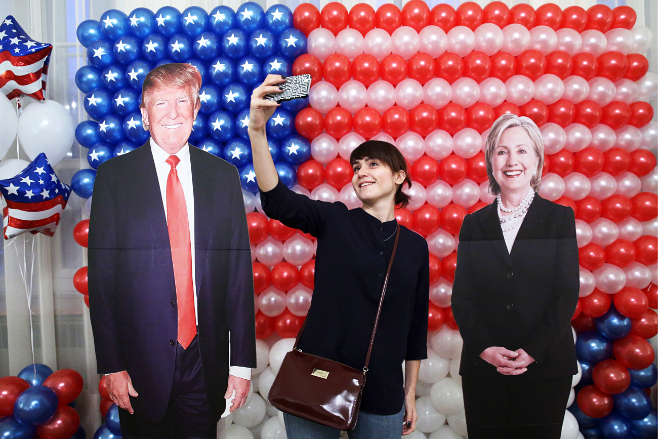 Una donna scatta un selfie tra due figure di cartone rappresentanti Donald Trump e Hillary Clinton.
