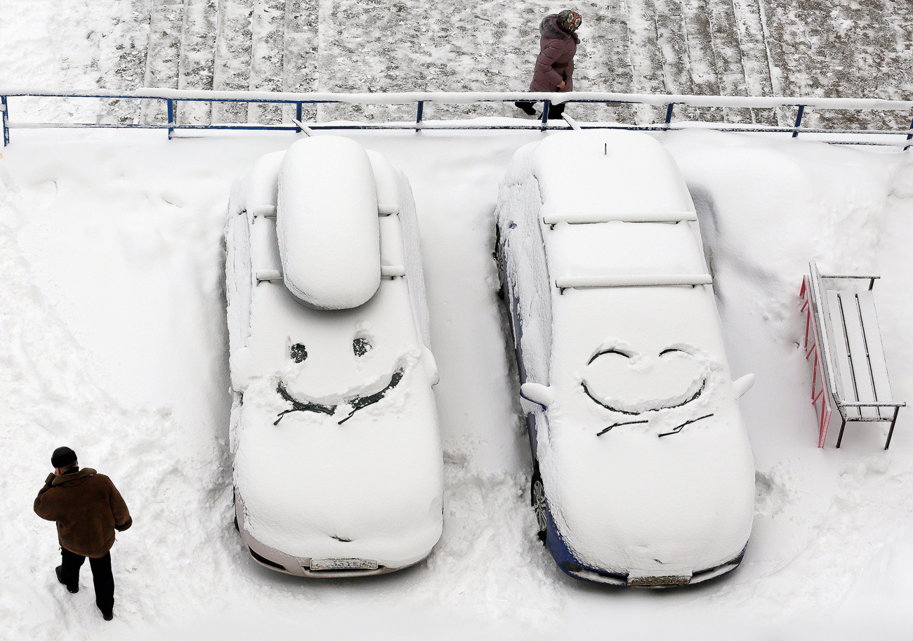Паркирани авотомобили со насликано лице на нивните ветробрани по снежните врнежи во Краснојарск, Сибир, Русија.