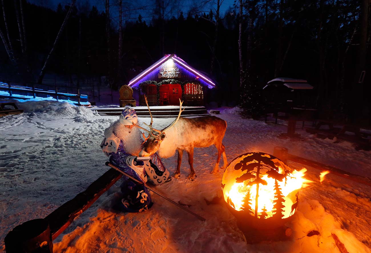 A man dressed as Ded Moroz (Father Frost, Russian equivalent of Santa Claus), sits by the fire with a reindeer Yakut, marking winter solstice at the Royev Ruchey Park of Flora and Fauna in the Siberian Taiga wood in the suburbs of Krasnoyarsk (2,500 miles east from Moscow).