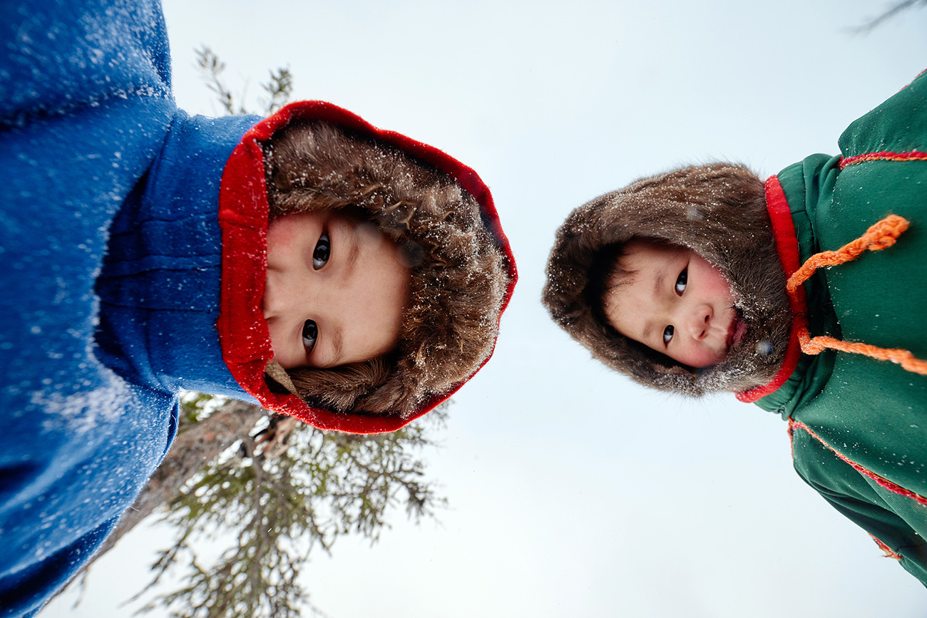 Directly below view of the Nenets kids in fur hats looking at camera against sky background, Yamal peninsula, Russia