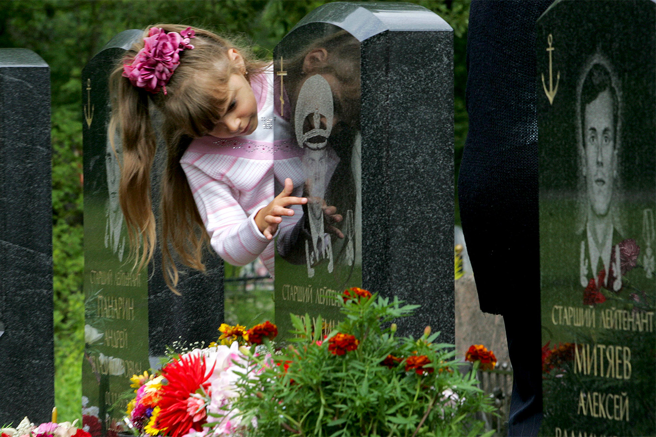 Seven-year-old Kristina Yerakhtina touches the tombstone of her father Sergei Yerakhtin Kursk nuclear submarine's officer at Serafimovskoye cemetery in St.Petersburg. Seven-year-old Kristina Yerakhtina touches the tombstone of her father Sergei Yerakhtin, Kursk nuclear submarine's officer, at Serafimovskoye cemetery in St.Petersburg, August 12, 2005. Russia marks five years since the loss of 118 sailors when the nuclear submarine Kursk went down in the Barents Sea after a torpedo exploded on board.