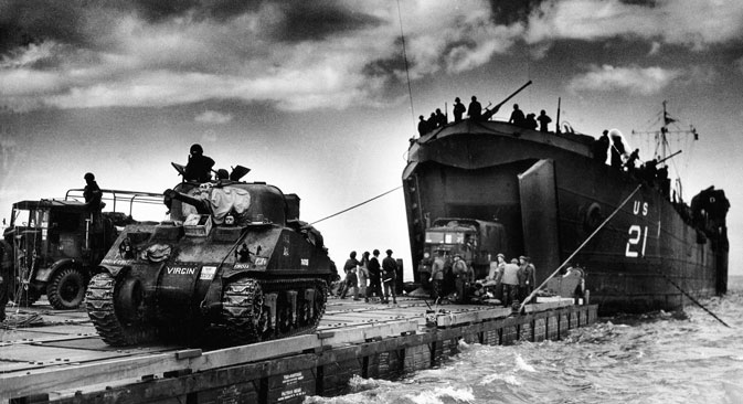 The U.S. Coast Guard manned USS LST-21 unloads British Army tanks and trucks onto a "Rhino" barge during the early hours of the invasion on Gold Beach. 6th June 1944. Normandy, France. Source: Source: UllsteinBild / Vostock_photo