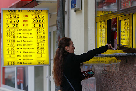 A woman hands over money to a shop employee near a board showing currency exchange rates in Kiev November 12, 2014. Ukraine's central bank said on Wednesday it may soften its policy on mandatory sales of foreign currency income on the domestic market, to encourage companies to bring more dollars into the country. Source: Reuters