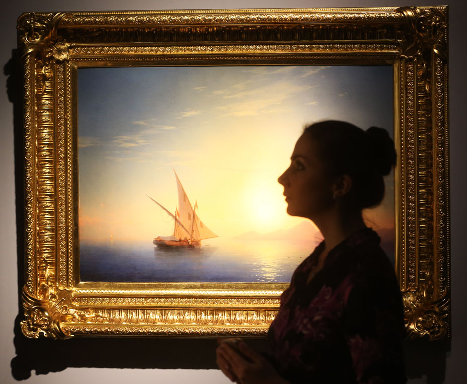 Eine junge Frau steht neben dem Bild „Sonnenuntergang auf Ischia“ von Iwan Aiwasowski. Das Bild ist Teil der Ausstellung „Russische Künstlerschätze: von Ikonen bis zur Moderne“ im Moskauer Kunstzentrum.