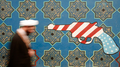 An Iranian cleric walks past a mural on the wall of the former U.S. embassy in Tehran
