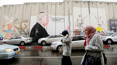Палестинцы в Вифлееме проходят мимо граффити, изображающих президента США Дональда Трампа

