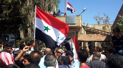 Сирийцы держат флаг своей страны на площади города Тафас в провинции Дараа после того, как населённый пункт перешёл под контроль правительственных сил