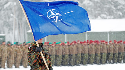Немецкий военнослужащий с флагом НАТО в руках на военной базе в Рукле