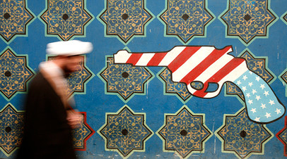An Iranian cleric walks past a mural on the wall of the former U.S. embassy in Tehran
