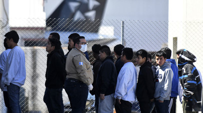 Сотрудник иммиграционной службы в защитной маске рядом с мигрантами, депортированными из Соединённых Штатов, Гватемала, март 2020 года