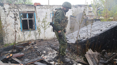 Военнослужащий Народной милиции ДНР осматривает сгоревший дом в посёлке Шахты