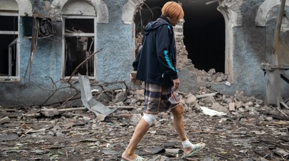 Женщина на фоне разрушенного здания после обстрела со стороны ВСУ в городе Брянки в ЛНР